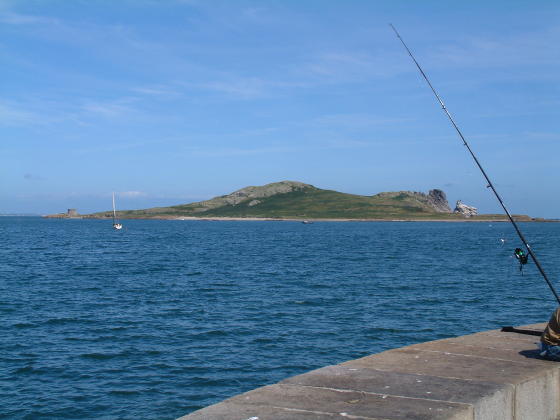 Looking across blue water to an island, with a fishing rod in the right foreground